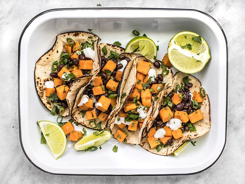Overhead view of sweet potato tacos in a serving dish with lime and cilantro
