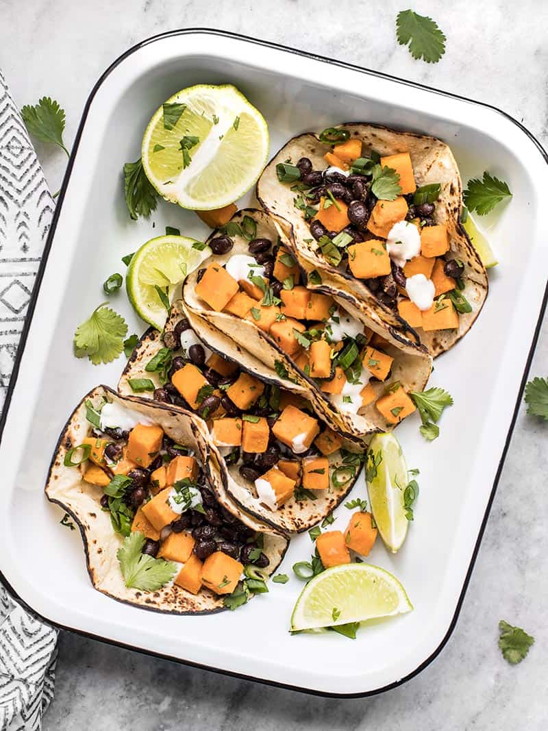 Overhead view of four sweet potato tacos in a white dish with limes and cilantro