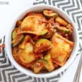 A bowl of zucchini sausage ravioli with sauce and a fork.