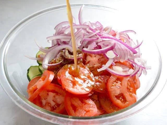 Dressing being poured onto sliced vegetables in a glass bowl