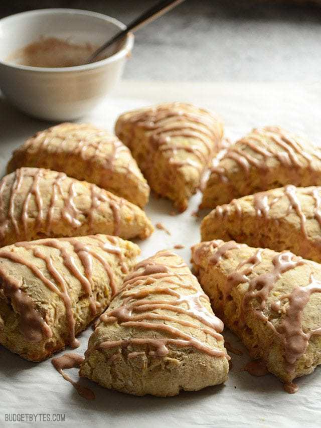 Inspired by a fresh baked apple pie, these Apple Pie Scones are flavored with cinnamon, ginger, and bits of shredded fresh apple. Budetbytes.com Side view of Apple Pie Scones with a bowl of glaze in the back
