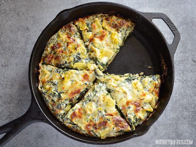 Creamy Spinach Artichoke Pizza in a cast iron skillet, one slice removed