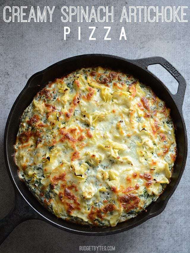 A rich and garlicky spinach cream sauce, artichoke hearts, and melty mozzarella make this thick crust Spinach Artichoke Pizza ultra indulgent! Budetbytes.com Overhead view of a Creamy Spinach Artichoke Pizza cooked in a cast iron pan, title text at the top