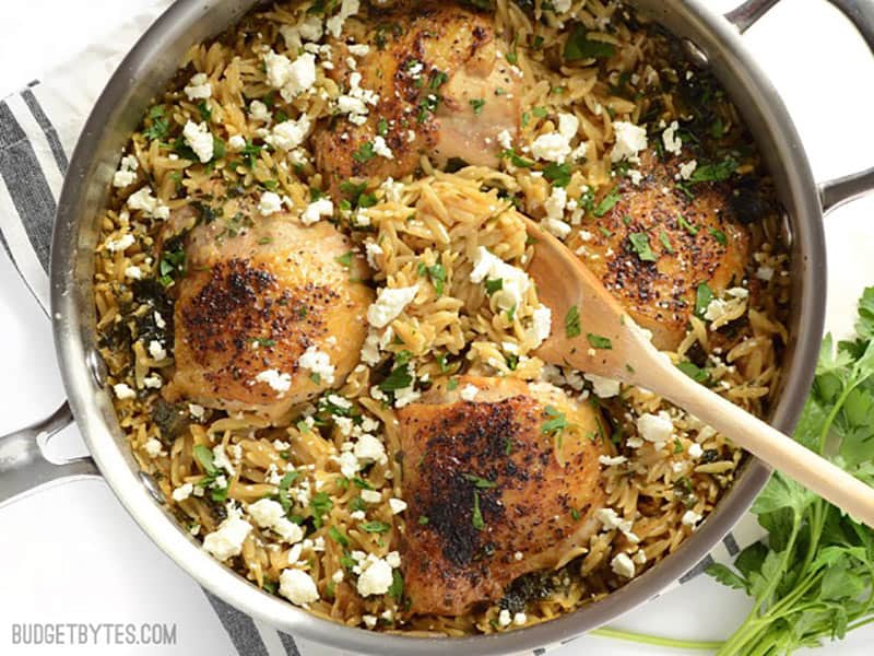 Overhead view of lemon pepper chicken with orzo in the skillet with a wooden spoon