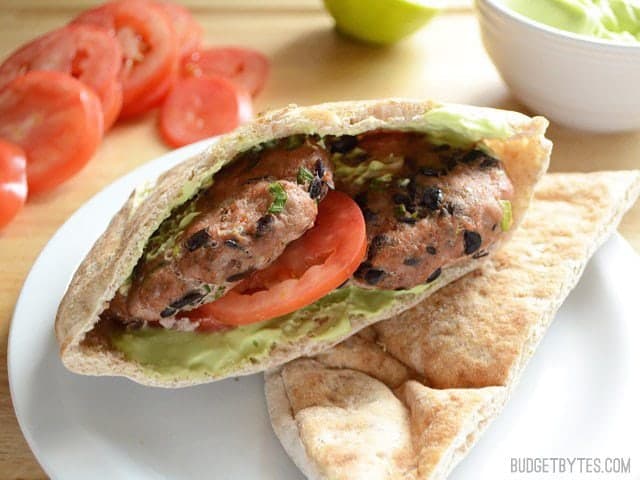 Two Cooked Mini Black Bean Turkey Burgers in a pita with avocado and tomato