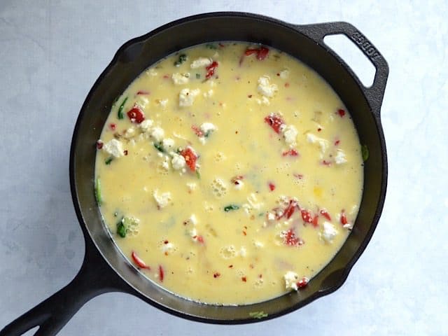 Eggs poured on top of vegetables and cheese in the skillet