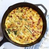 A frittata with roasted red peppers and feta on a cast iron pan.