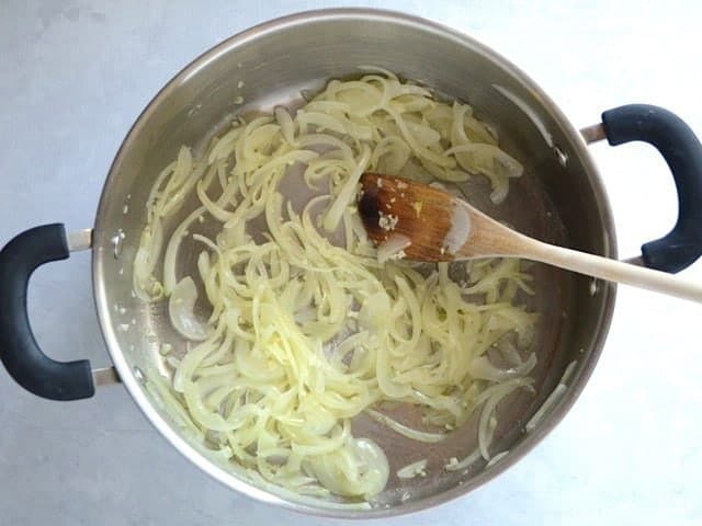Sautéed Onions and Garlic in a large pot with a wooden spoon