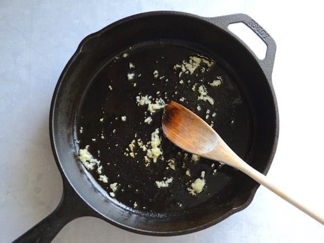 Sautéed Garlic in a cast iron skillet with a wooden spoon