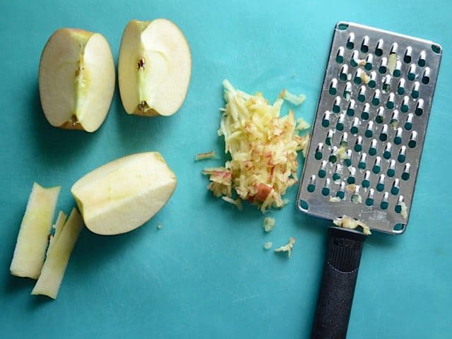 An apple quartered, cored, and shredded next to a cheese grater