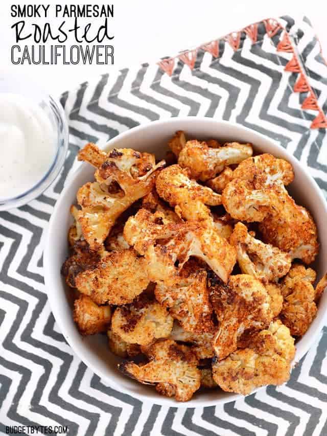 Smoky Parmesan Roasted Cauliflower is an easy, smoky, and savory side dish or snack for dipping in your favorite sauces. Step by step photos. Budetbytes.com A bowl of Smoky Parmesan Roasted Cauliflower on a zig zag napkin, title text at the top