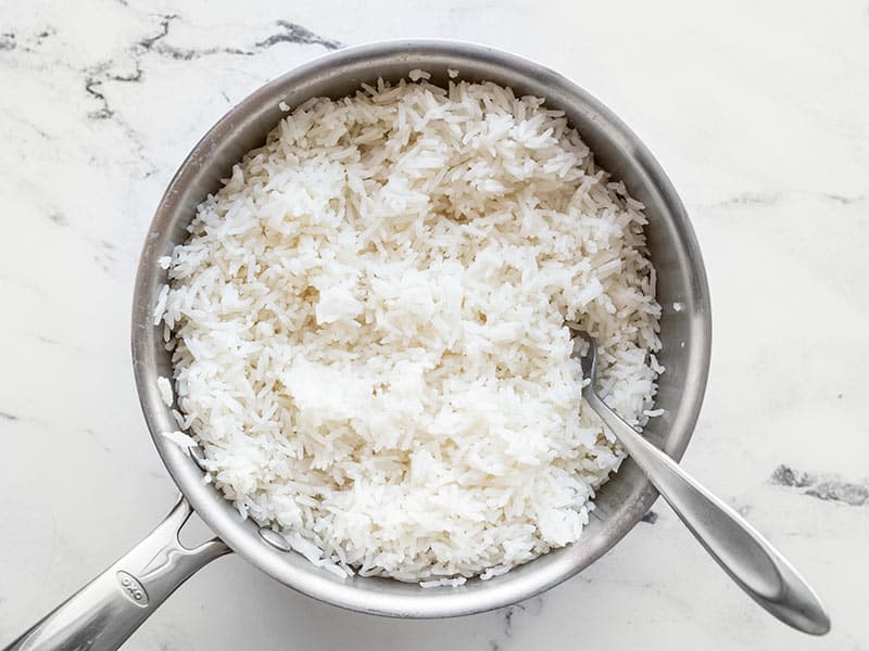 Cooked rice in a sauce pot, fluffed with a fork