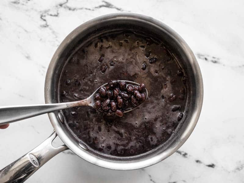 Seasoned and heated black beans in a sauce pot