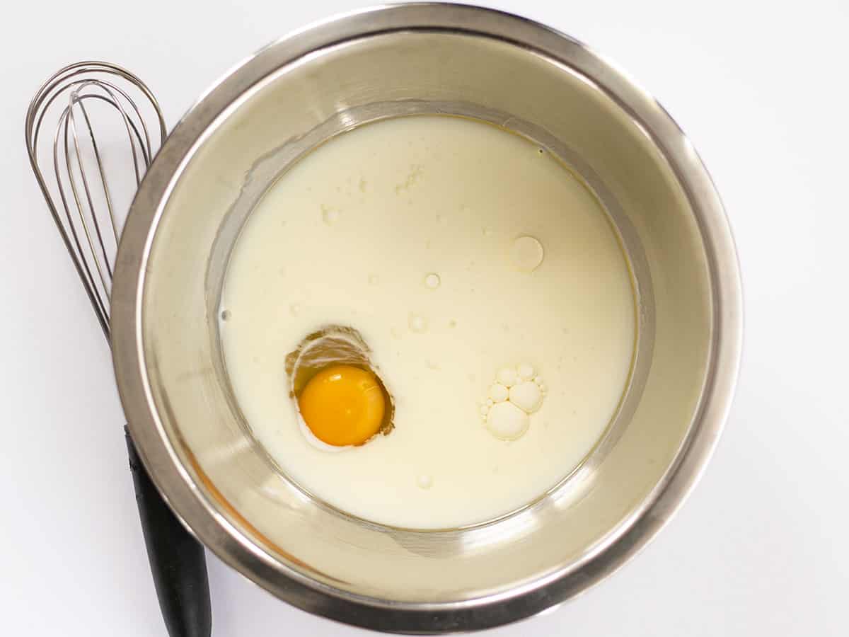 Milk, egg, and oil in a metal bowl with a whisk on the side.