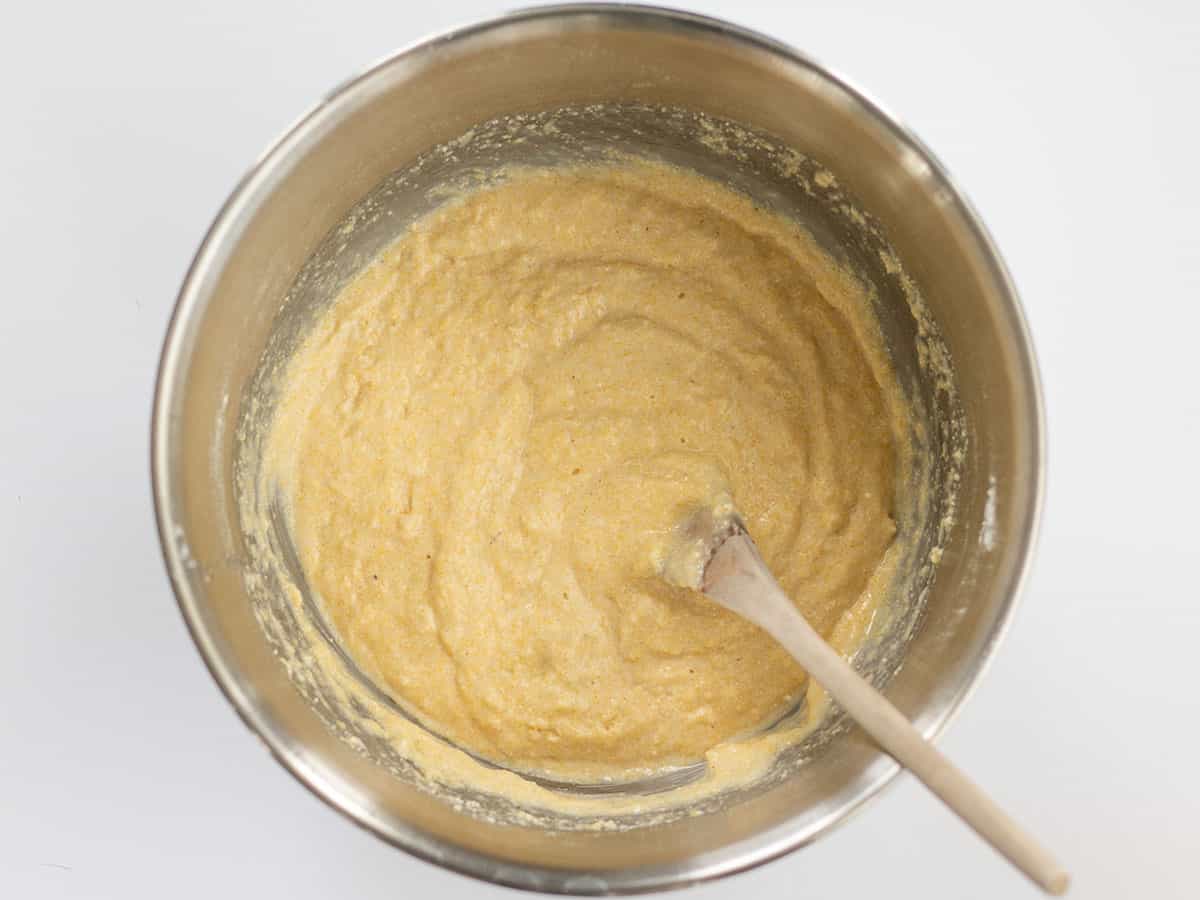 Mixed cornbread batter in a metal bowl with a wooden spoon.