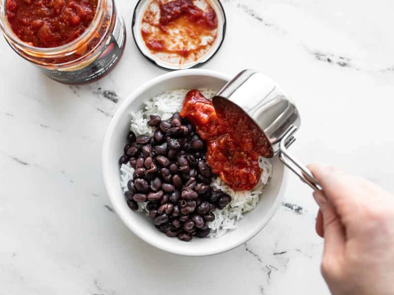 build burrito bowls - salsa being scooped into a bowl with rice and beans