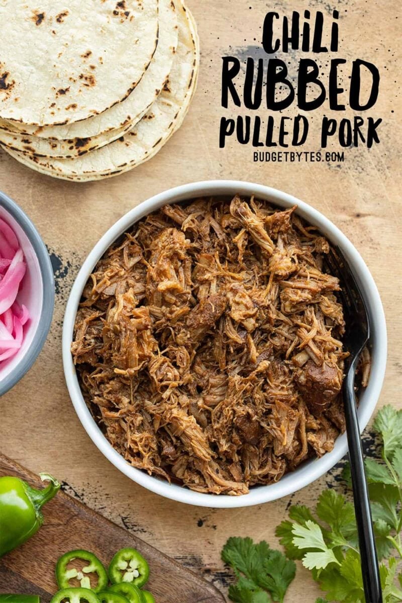 Overhead view of a bowl of pulled pork with tortillas and onions on the side