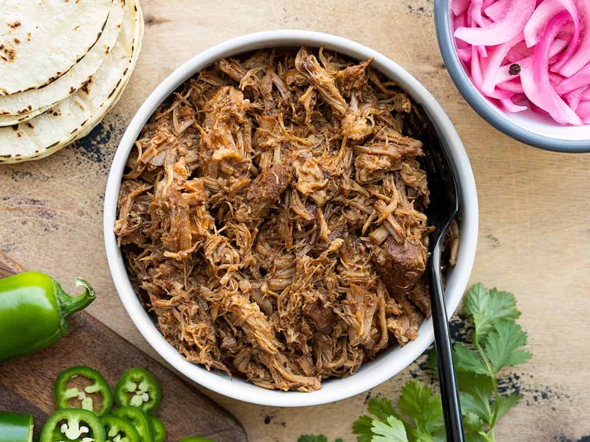 Overhead view of a bowl full of chili rubbed pulled pork with taco fixings on the sides