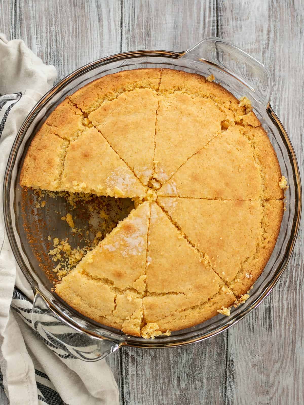 Overhead view of cornbread in a glass baking dish with one piece cut out.