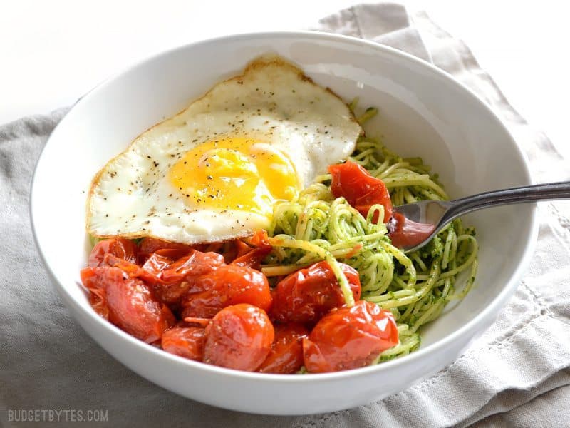 Vibrant green parsley pesto pasta pairs perfectly with sweet blistered cherry tomatoes and a the creamy yolk of a fried egg. Simple, delicious food. Budetbytes.com Side view of a bowl of parsley pesto pasta with blistered tomatoes and a fried egg on top