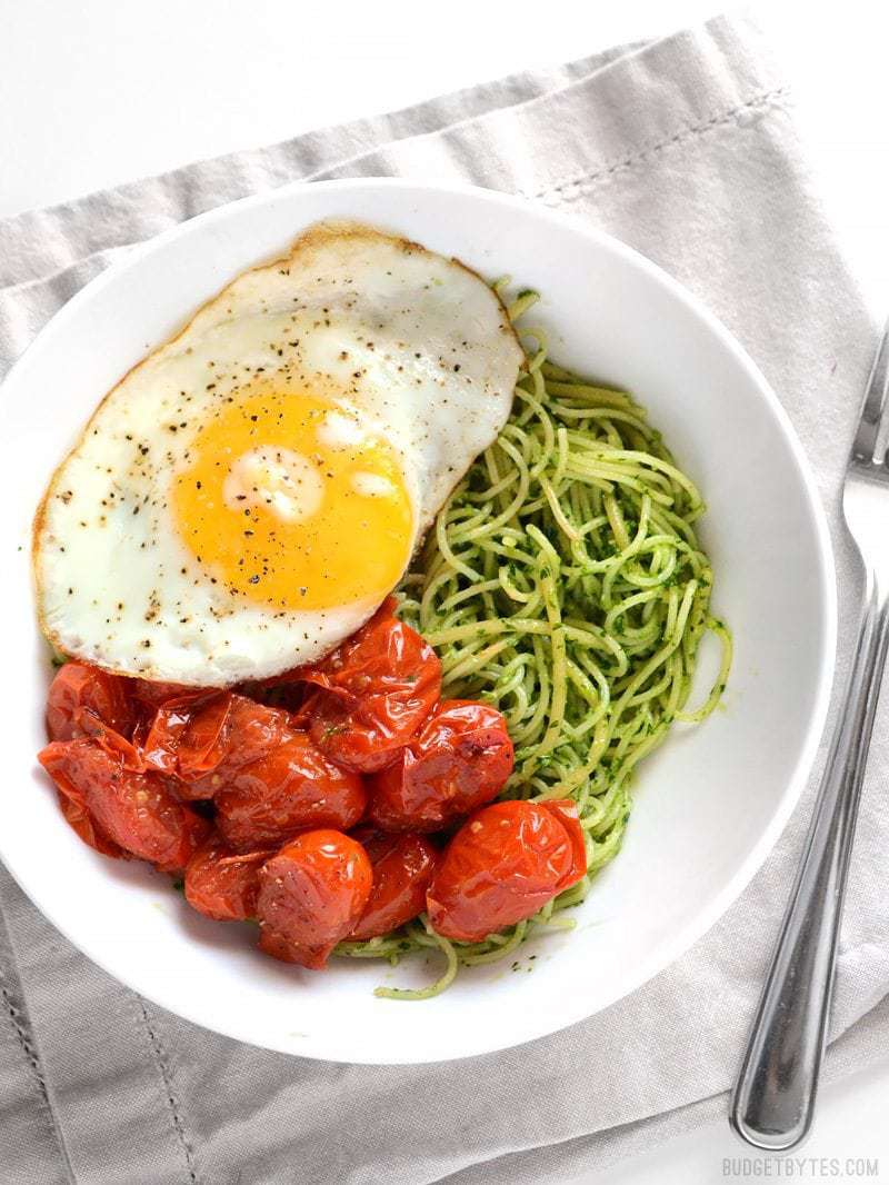 Overhead view of a bowl full of parsley pesto pasta with blistered tomatoes and a fried egg