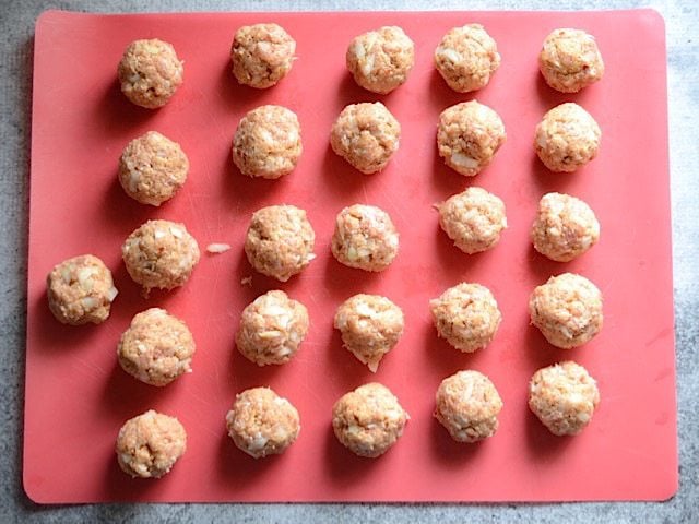 Raw shaped Meatballs on a red cutting board