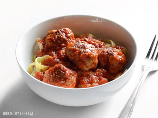 Side view of a bowl full of pasta with meatballs and marinara