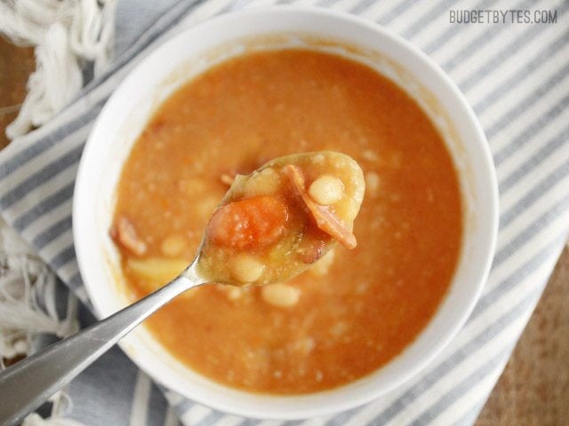 This hearty Bacon Bean and Potato Soup is extra thick with both beans and potato, plus enough bacon and vegetables to give each bowl plenty of flavor! Budetbytes.com Close up of a spoonful of Bacon Bean and Potato Soup, the bowl in the background