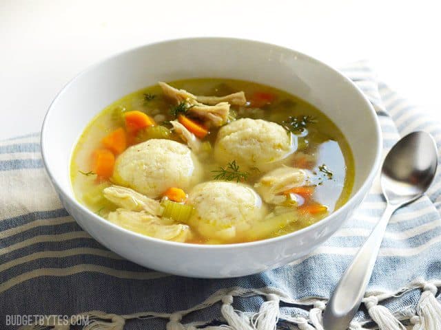 Front view of a bowl of Matzo Ball Soup with a spoon on the side