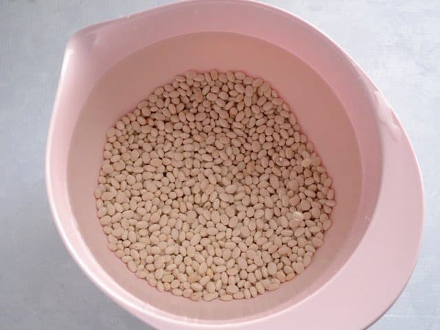 Uncooked navy beans in a bowl full of water