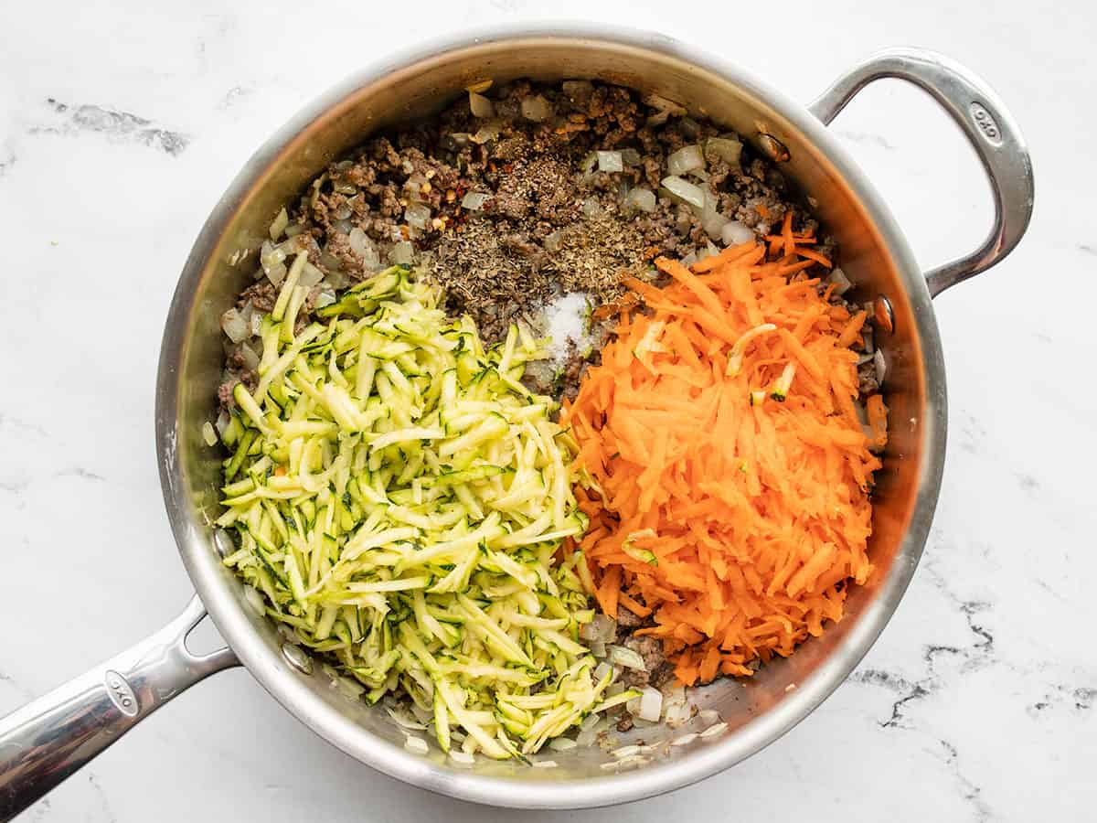 Shredded vegetables added to the skillet with the meat