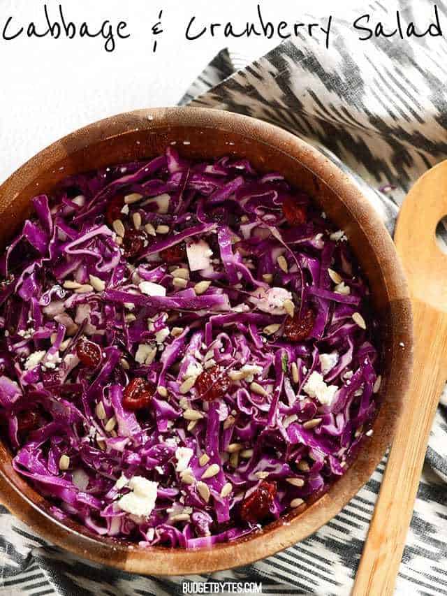 Overhead view of a wooden bowl filled with Cranberry and Cabbage Salad. Title text at the top.