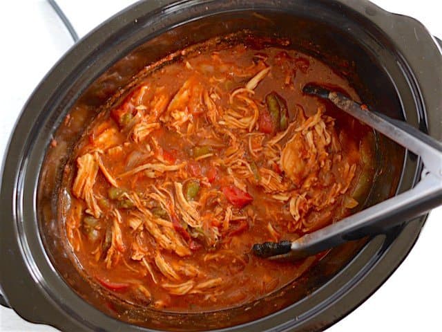 Shredded chicken in the slow cooker with tongs