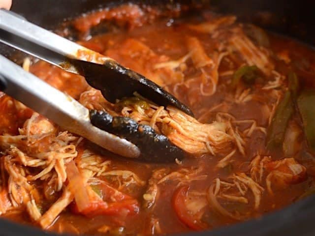 Tongs picking up shredded chicken out of the slow cooker