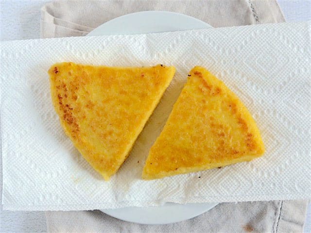 Two fried polenta slices on a paper towel