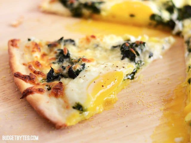 One slice of Eggs Florentine Breakfast Pizza on a wooden cutting board