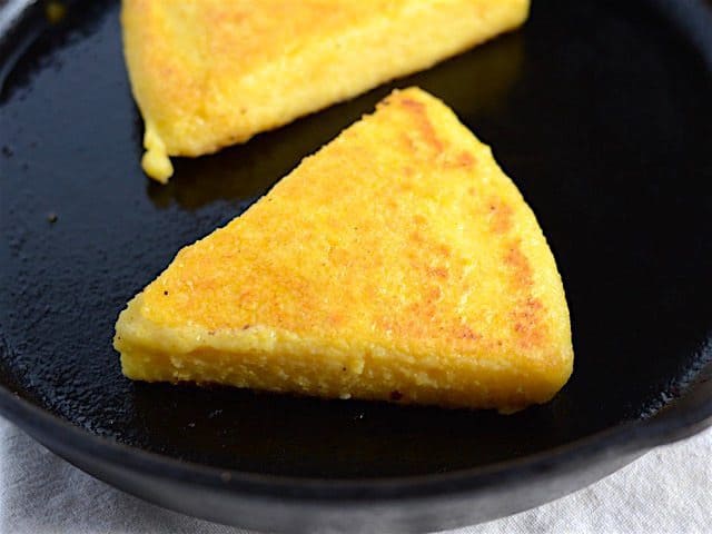 Two fried polenta slices in a cast iron skillet