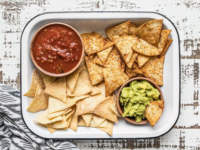 A baking dish full of Homemade Baked Tortilla Chips with bowls of salsa and guacamole