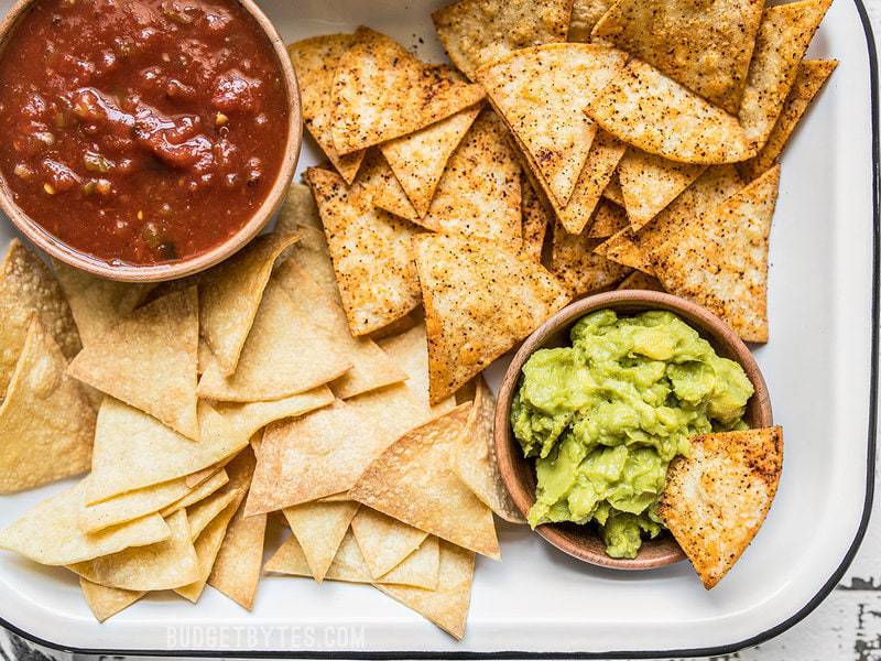 Close up of Homemade Baked Tortilla Chips with bowls of salsa and guacamole