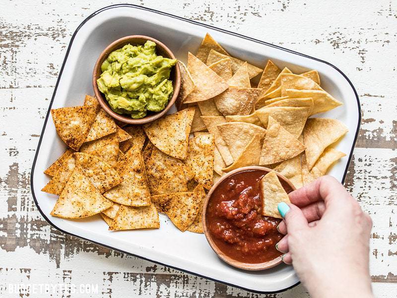 A hand dipping a Homemade Baked Tortilla Chip into a bowl of salsa