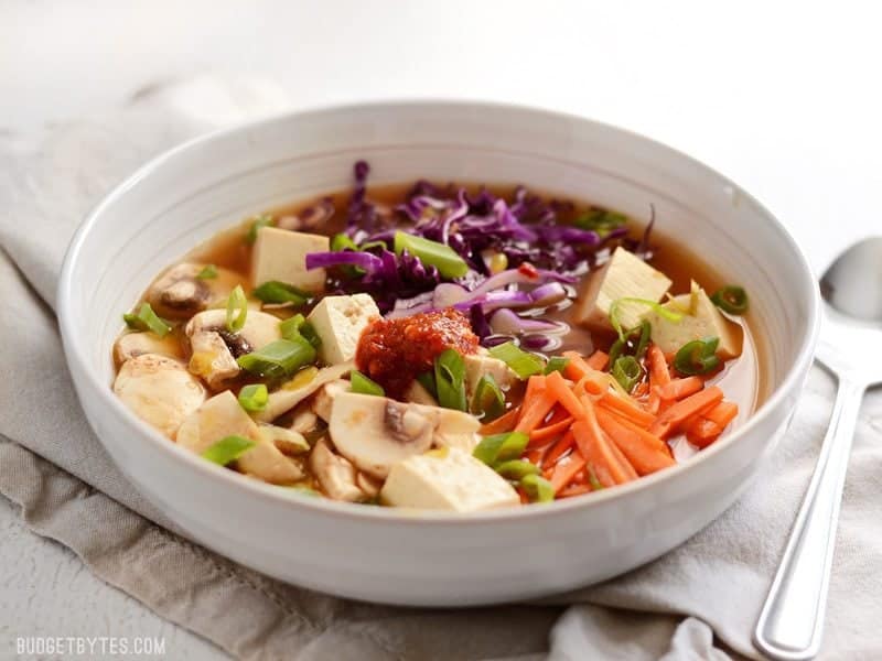 Front view of a shallow bowl of vegetables and tofu with hot and sour soup broth