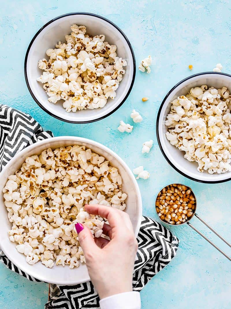 A hand picking up a handful of popcorn from a large bowl, two smaller bowls on the side