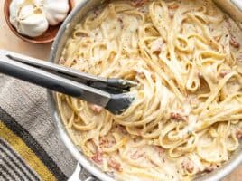 Overhead view of creamy pasta twirled around the tongs in the skillet.