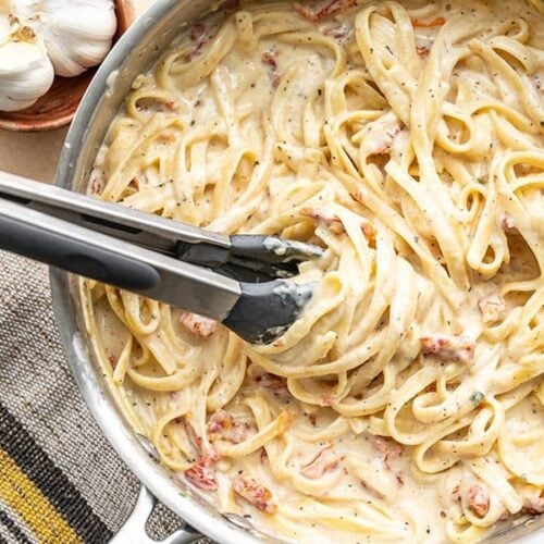 Overhead view of creamy pasta twirled around the tongs in the skillet.