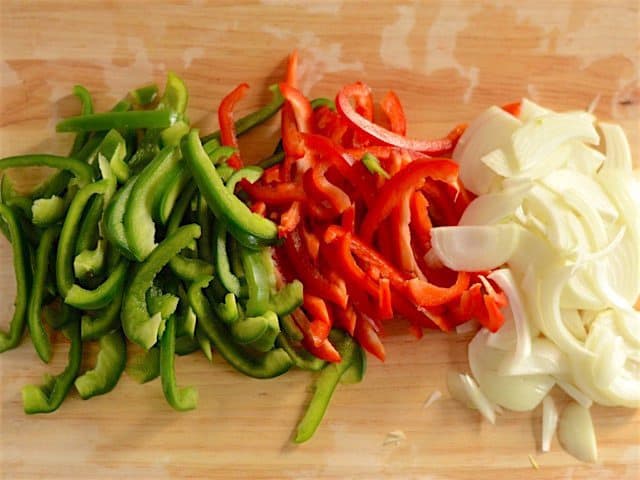 Sliced peppers and onions on a wooden cutting board