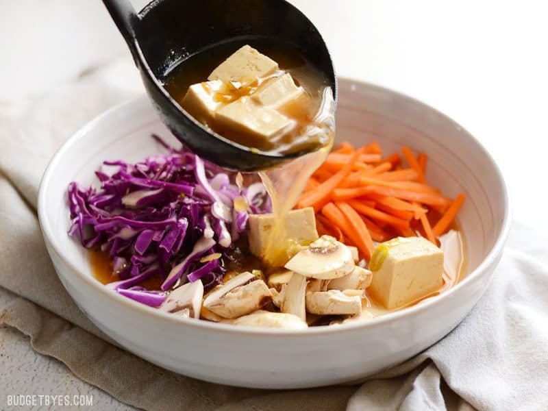 Broth being ladled over vegetables in the soup bowl