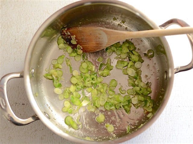 Green onion and ginger in a soup pot with a wooden spoon.