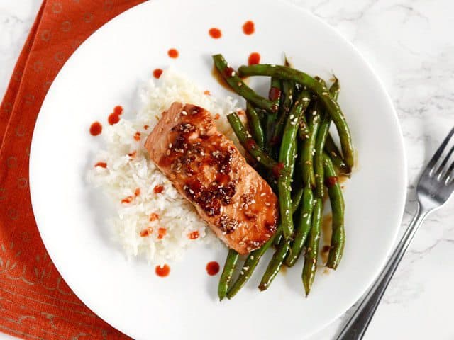 Sesame Glazed Salmon and Green Beans plated with jasmine rice and a drizzle of sriracha