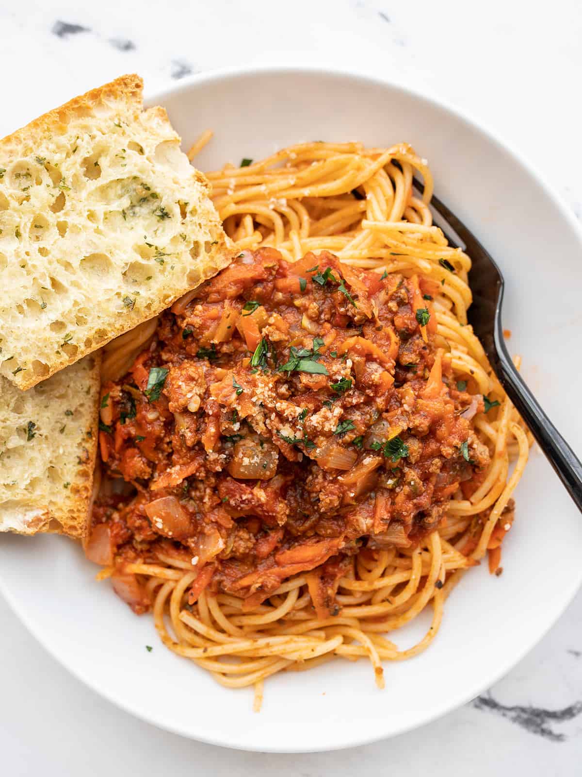 Overhead view of a bowl of spaghetti with hidden vegetable pasta sauce and garlic bread on the side