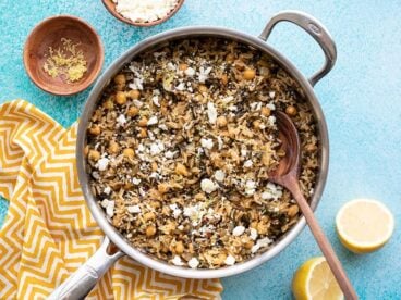 Skillet full of Spinach and Chickpea Rice Pilaf next to a cut lemon and small dish of feta, on a blue background